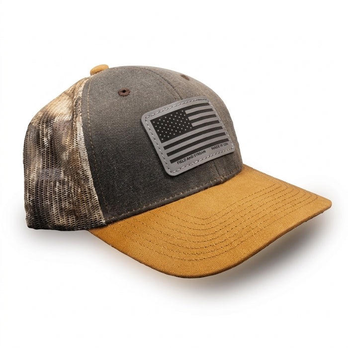 Trucker hat with gray front, camouflage mesh back, tan brim and black-and-gray American flag patch